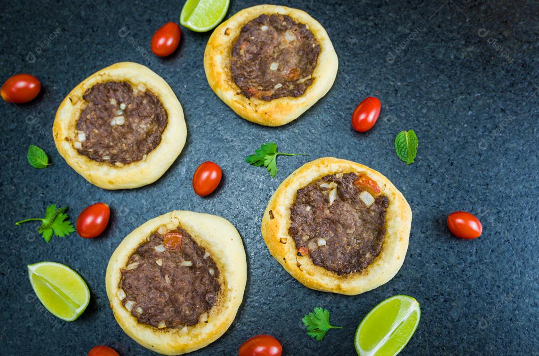 Deliciosa comida libanesa (árabe), esfihas legítimas em um fundo de granito preto com tomates, limões.