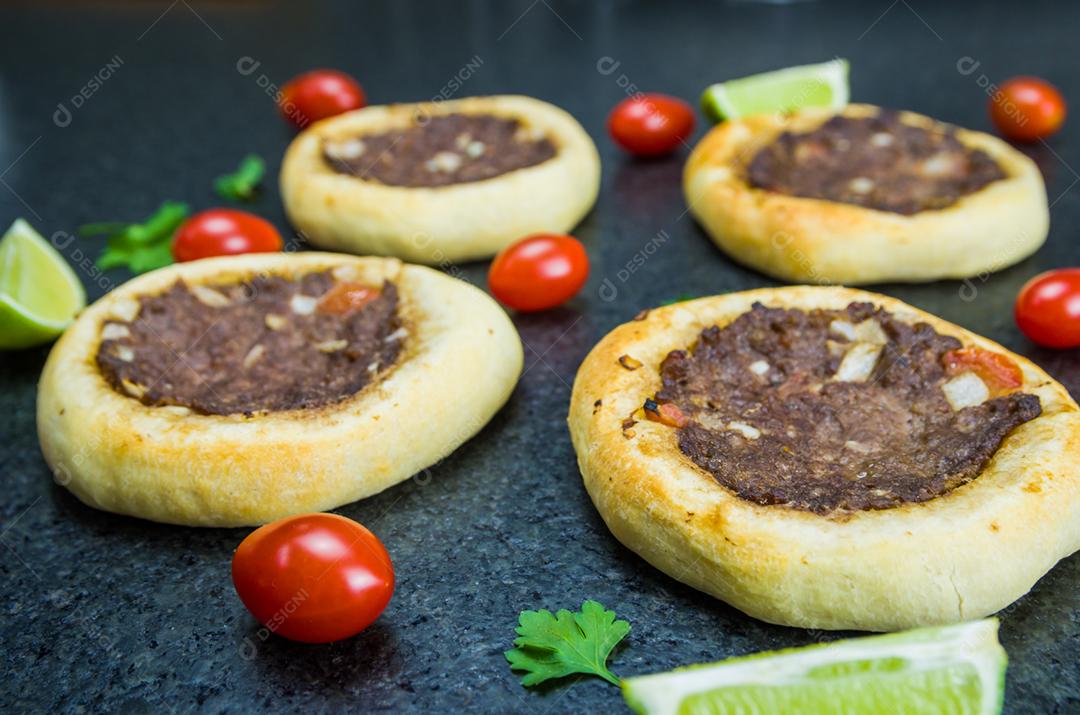 Deliciosa comida libanesa (árabe), esfihas legítimas em um fundo de granito preto com tomates, limões.