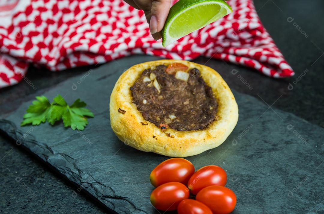 Deliciosa comida libanesa (árabe), espremendo limão em esfihas legítimas em um fundo de granito preto