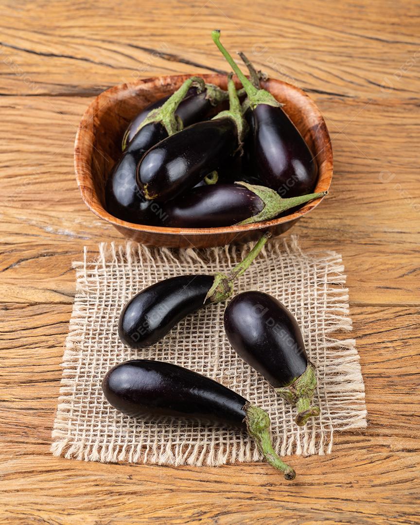 Pequenas berinjelas em uma tigela sobre a mesa de madeira