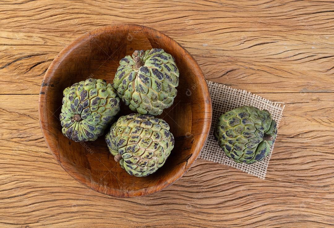 Maçãs de açúcar ou pinha em uma tigela sobre a mesa de madeira.