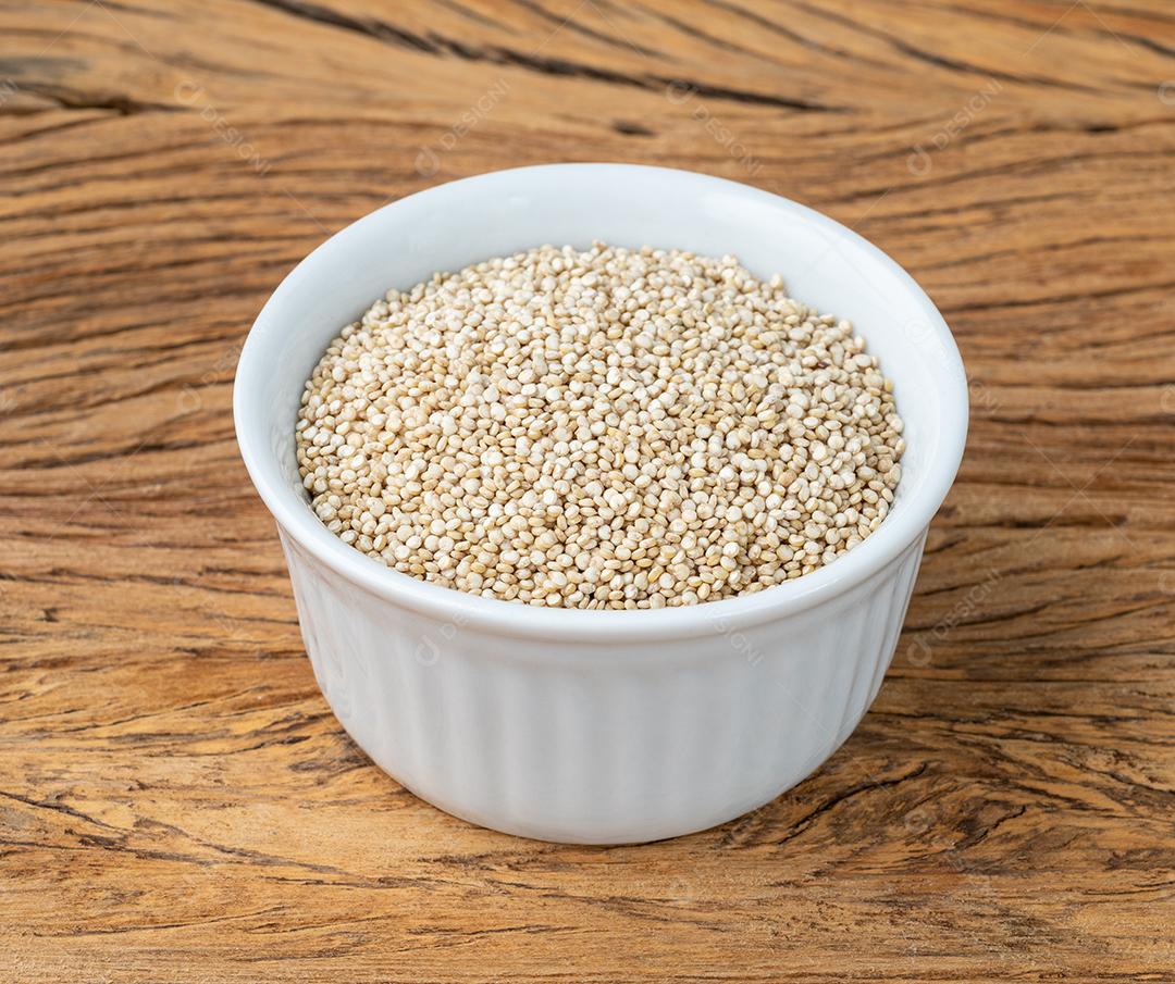 Grãos de quinoa crus em uma tigela sobre a mesa de madeira.