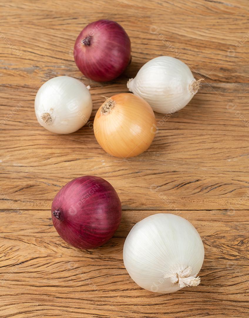 Red, white and golden onions on the wooden table.