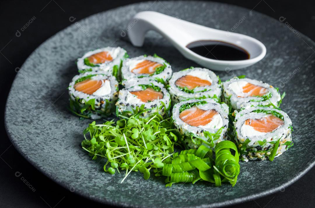 Sushi perfeito, cozinha tradicional japonesa. Delicioso uramaki com molho shoyo no prato decorado, fundo preto.