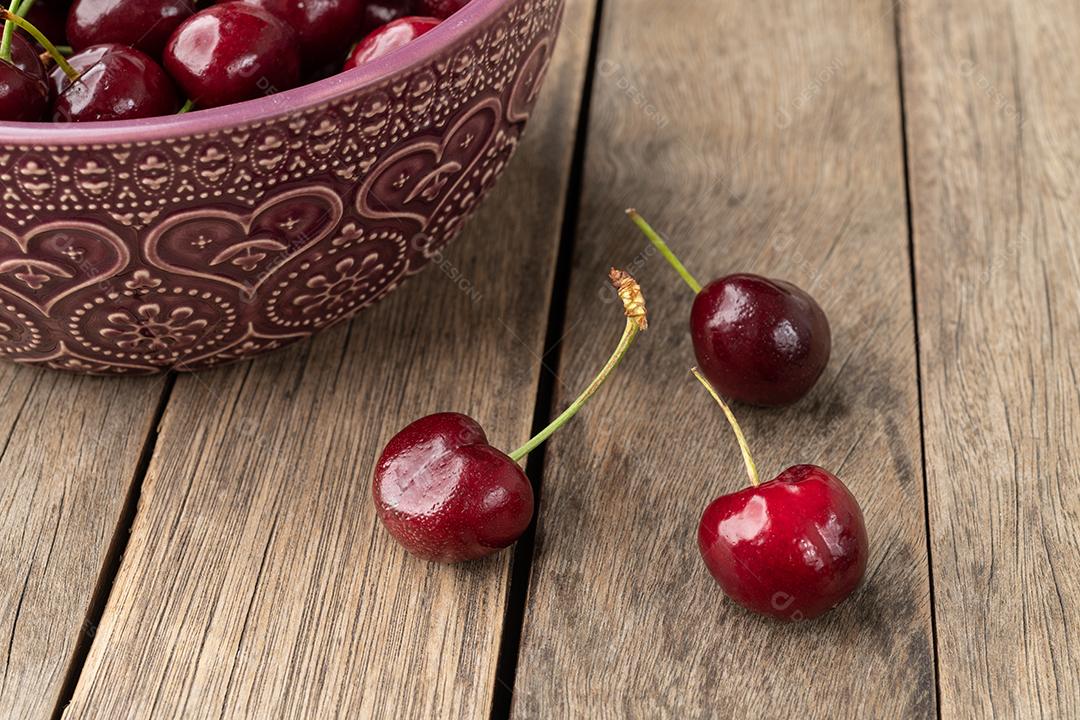 Cerejas vermelhas em uma tigela sobre a mesa de madeira.