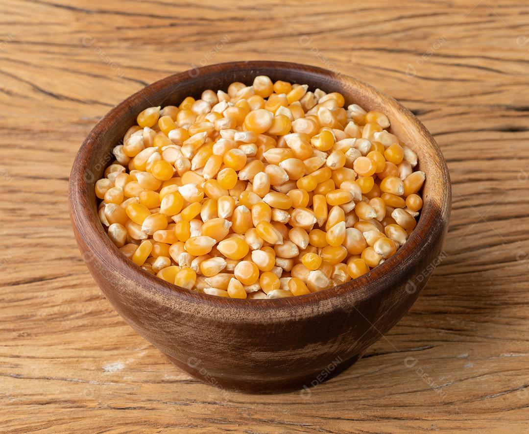 Grãos de milho ou pipoca secos em uma tigela sobre a mesa de madeira.