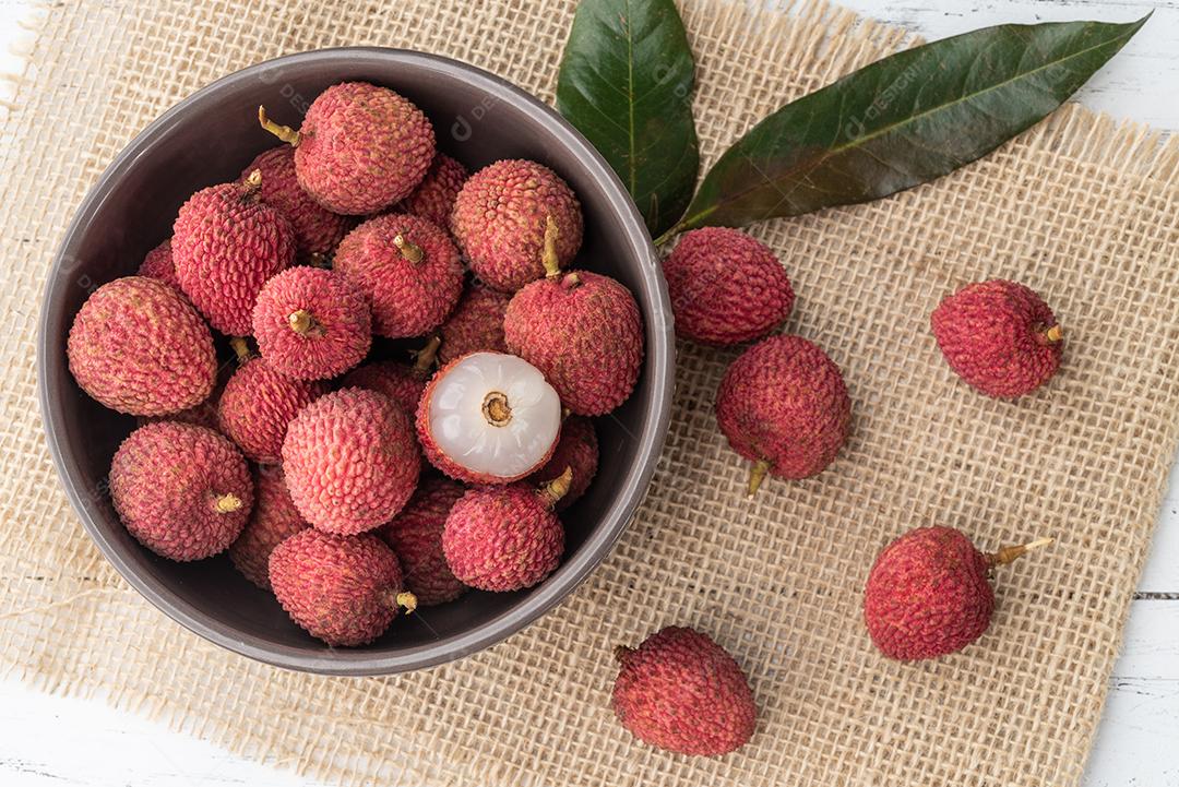 Lichias em uma tigela com frutas cortadas sobre a mesa de madeira.