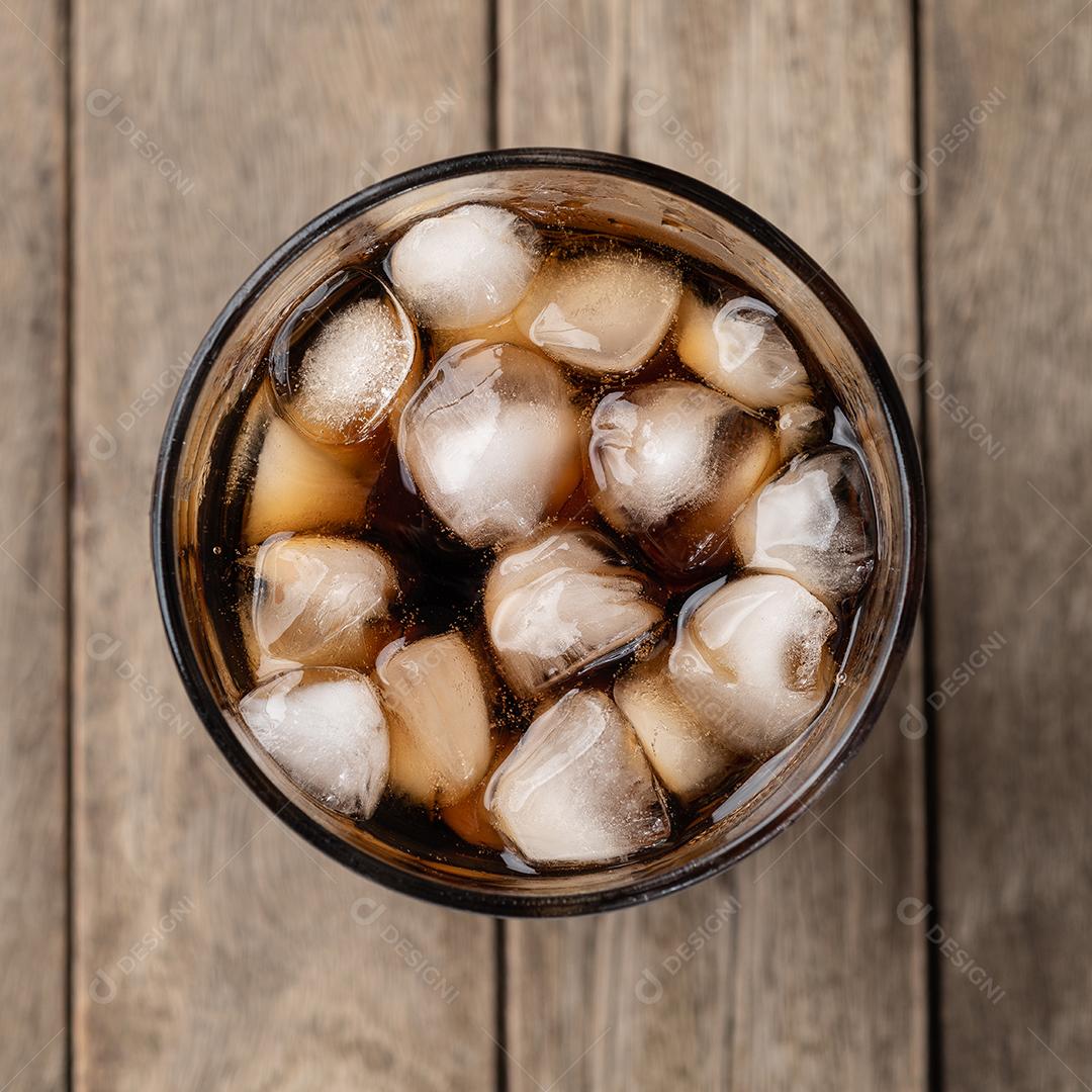 Refrigerante de cola, refrigerante em um copo com gelo sobre a mesa de madeira.