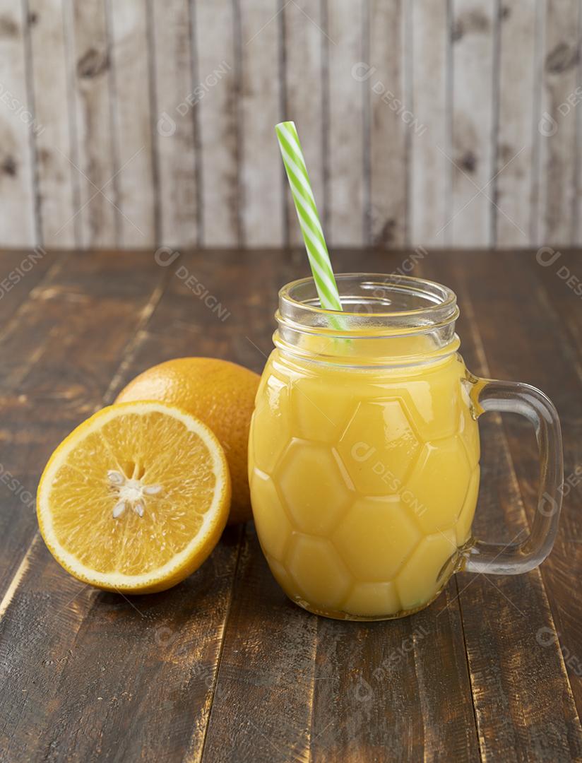 Suco de laranja com laranja fatiada sobre uma mesa de madeira.