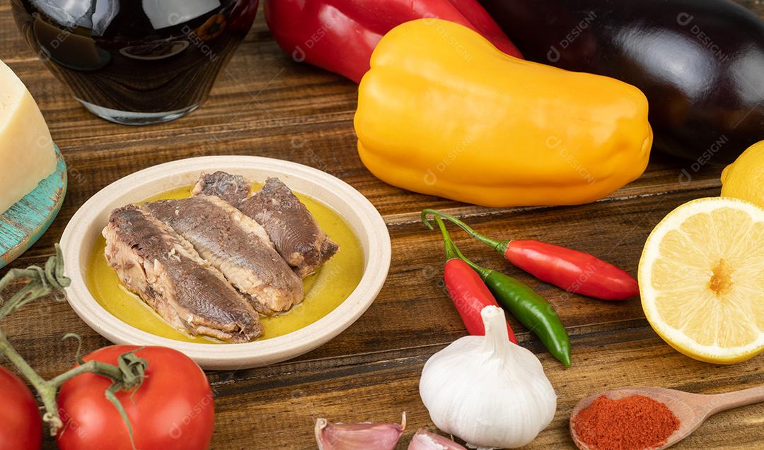 Peixe, tomate, pimentão, berinjela, azeite, limão siliciano, vinho, pimenta e alho sobre mesa de madeira. Comida mediterrânea.