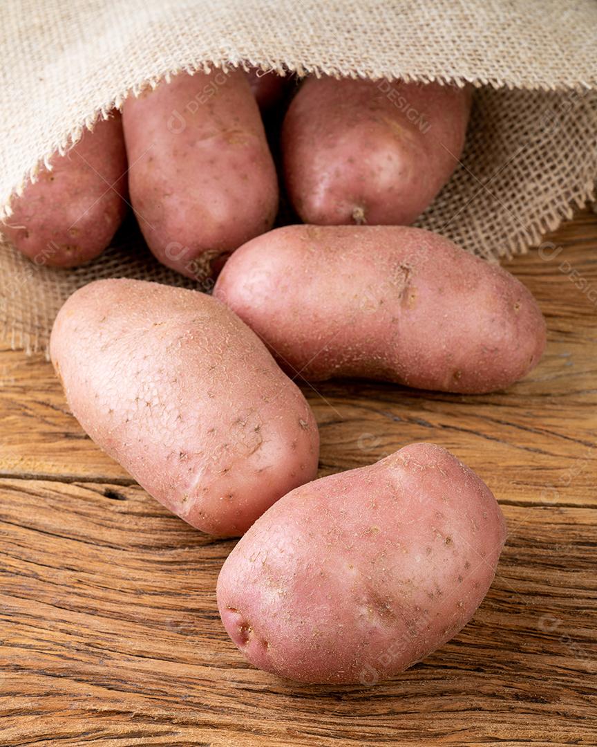 Batata vermelha em um saco sobre mesa de madeira.