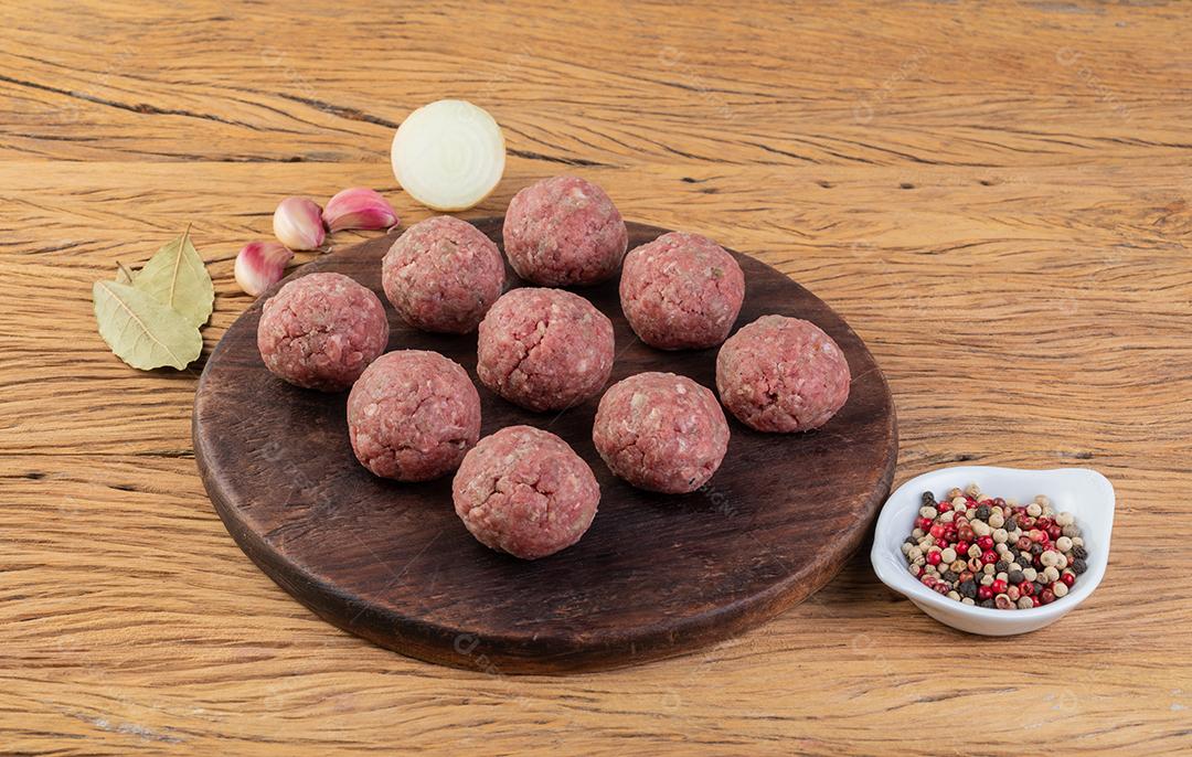 Almôndegas cruas sobre tábua de madeira com temperos.