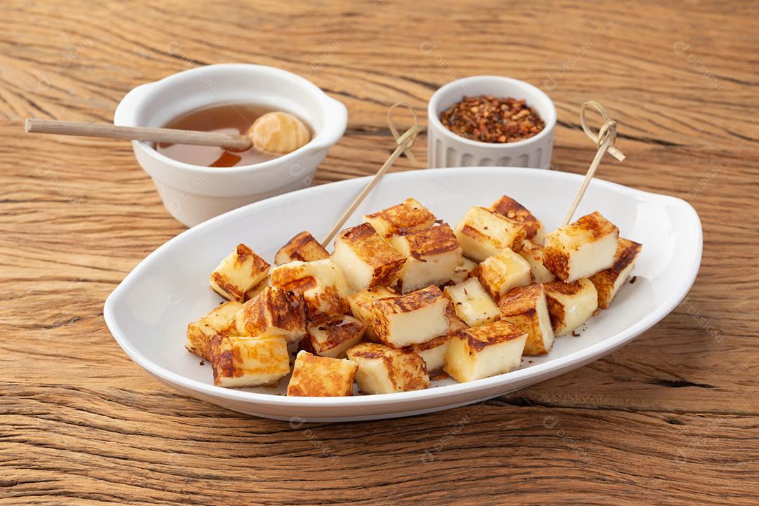 Renegar grelhado ou queijo Coalho com xarope de açúcar e pimenta em uma mesa de madeira.