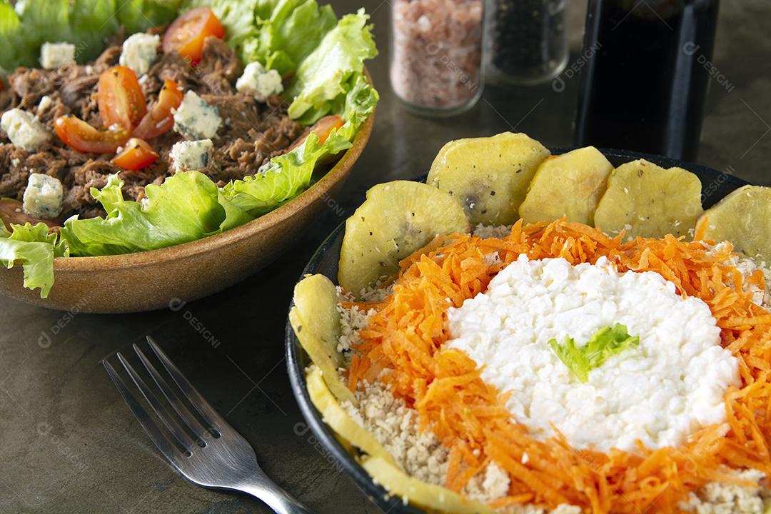 Saladas em tigelas coloridas, sal, pimenta e garrafa de azeite sobre fundo de pedra.