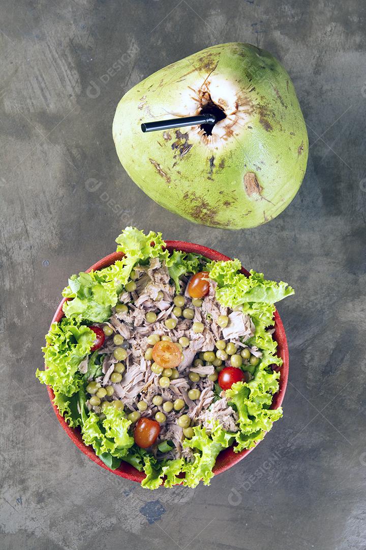 Salada em tigela colorida e coco verde sobre fundo de pedra.