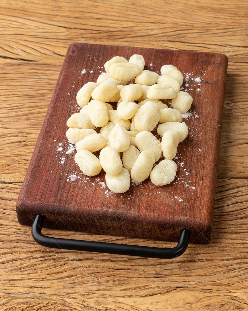 Nhoque de macarrão italiano cru em uma tábua sobre mesa de madeira.