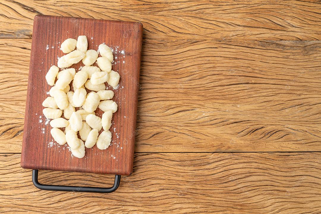 Nhoque de macarrão italiano cru em uma tábua sobre mesa de madeira