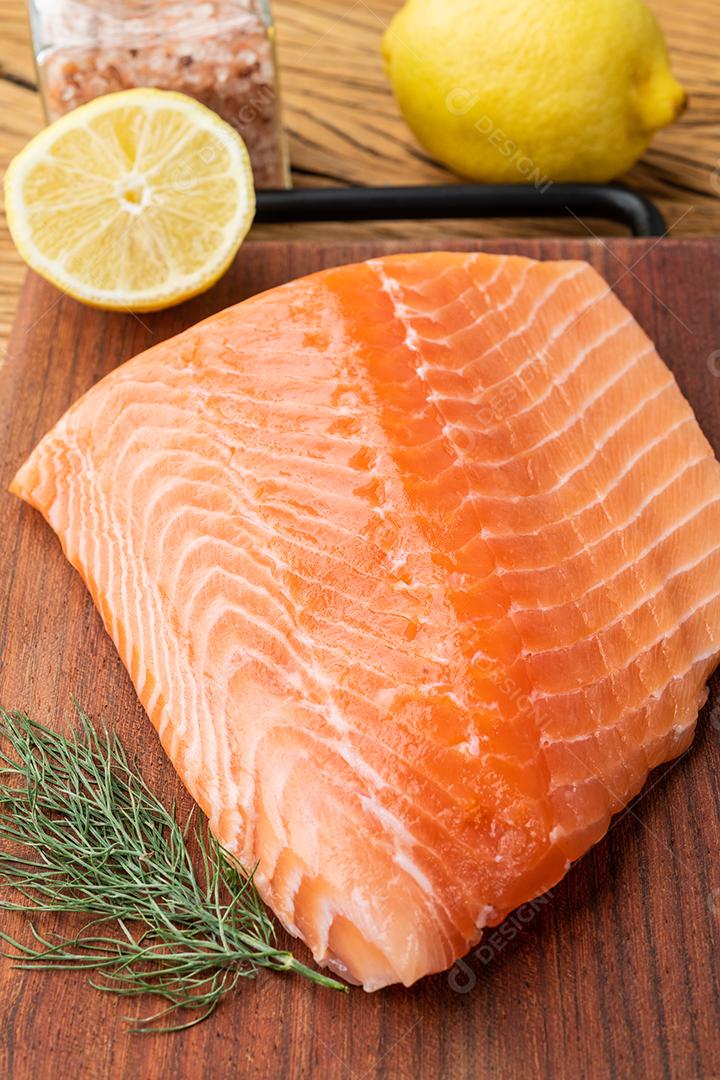 Filé de salmão cru com temperos sobre tábua de madeira.