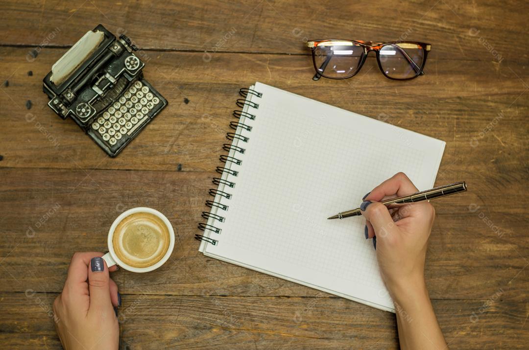 Jovem bebendo café sobre uma xicara de cafe caderno caneta