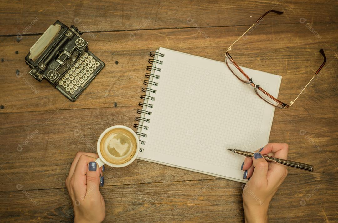 Jovem bebendo café sobre uma xicara de cafe caderno caneta