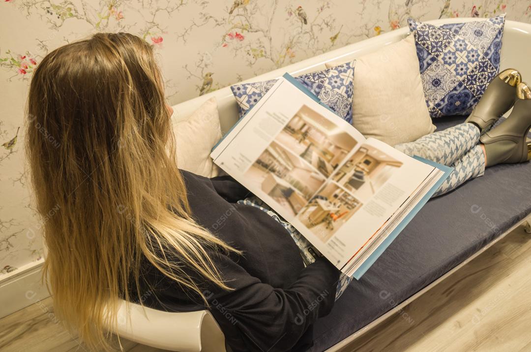 Jovem mulher loira deitado no sofá lendo livro