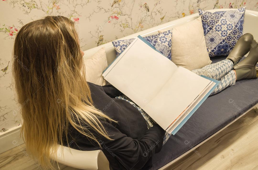 Jovem mulher loira deitado no sofá lendo livro