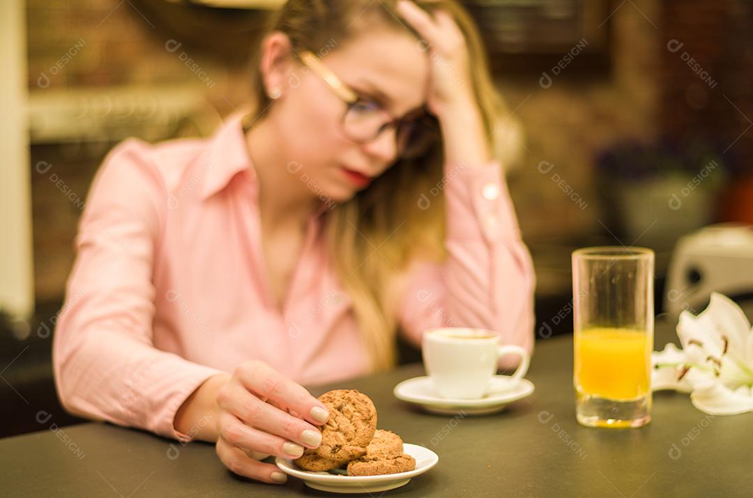 Mesa posta, café , biscoitos e suco com mullher preocupada com a mao na cabeça