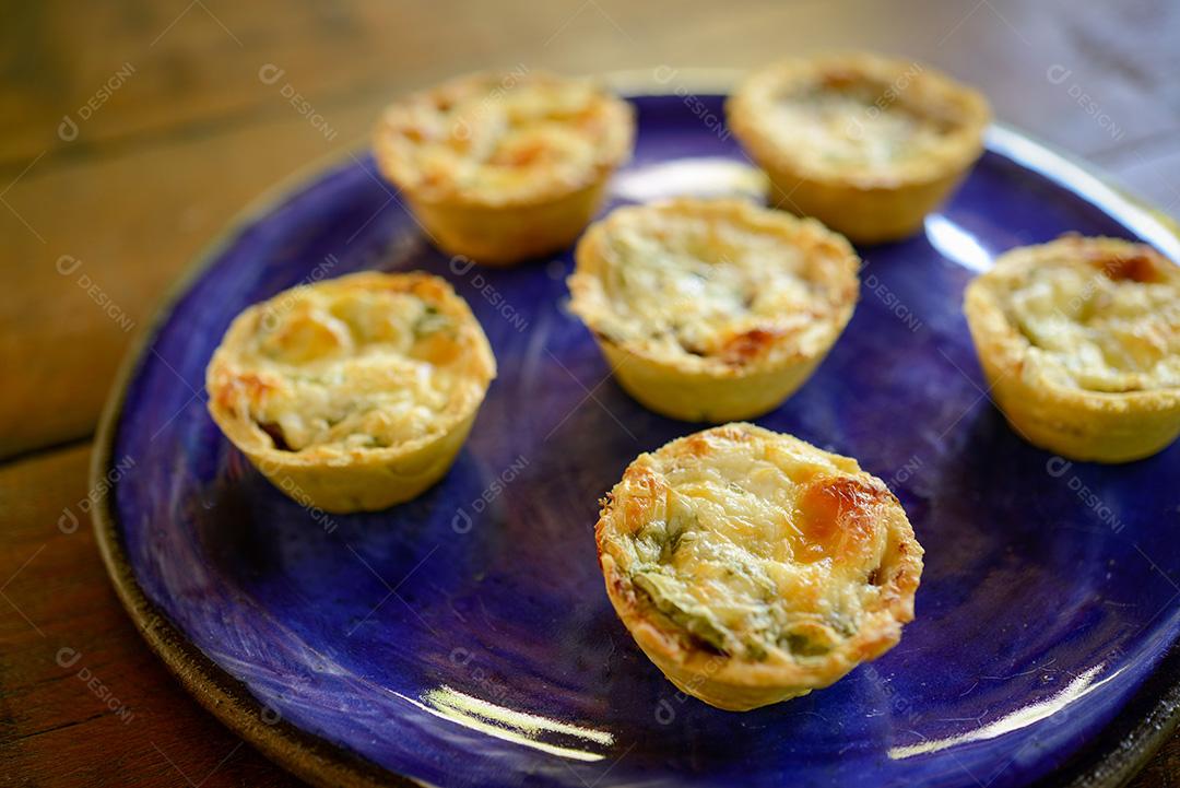 gastronomia brasileira. Tortas de queijo e carne seca com rúcula em prato artesanal na mesa de madeira.