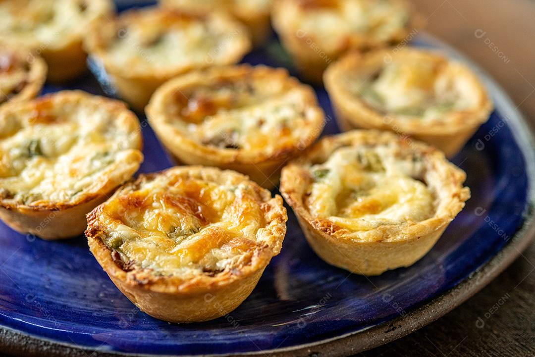 gastronomia brasileira. Tortas de queijo e carne seca com rúcula em prato artesanal na mesa de madeira.