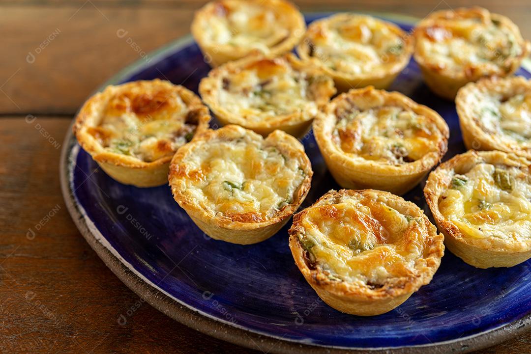 gastronomia brasileira. Tortas de queijo e carne seca com rúcula em prato artesanal na mesa de madeira.