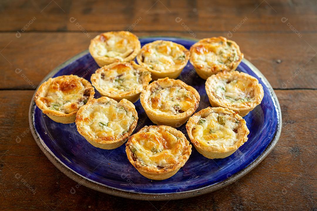 gastronomia brasileira. Tortas de queijo e carne seca com rúcula em prato artesanal na mesa de madeira.