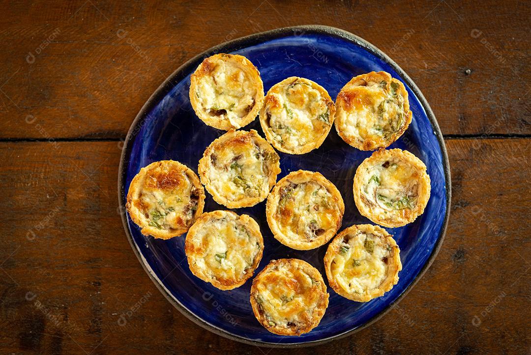 gastronomia brasileira. Tortas de queijo e carne seca com rúcula em prato artesanal na mesa de madeira.