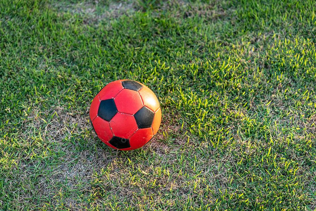Bola de futebol vermelha e preta no gramado.