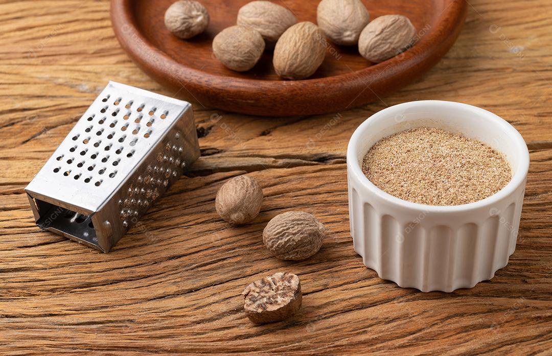 Noz-moscada com ralador sobre mesa de madeira. Nozes em uma tigela.