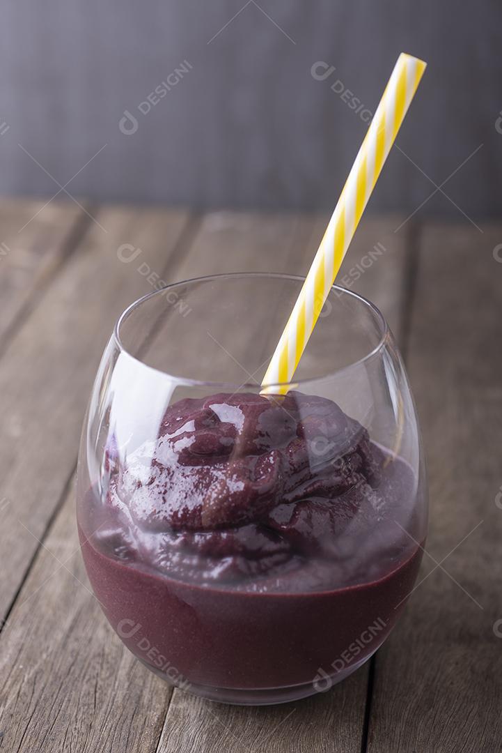 Suco típico de açaí brasileiro em um copo com palha sobre fundo de madeira.