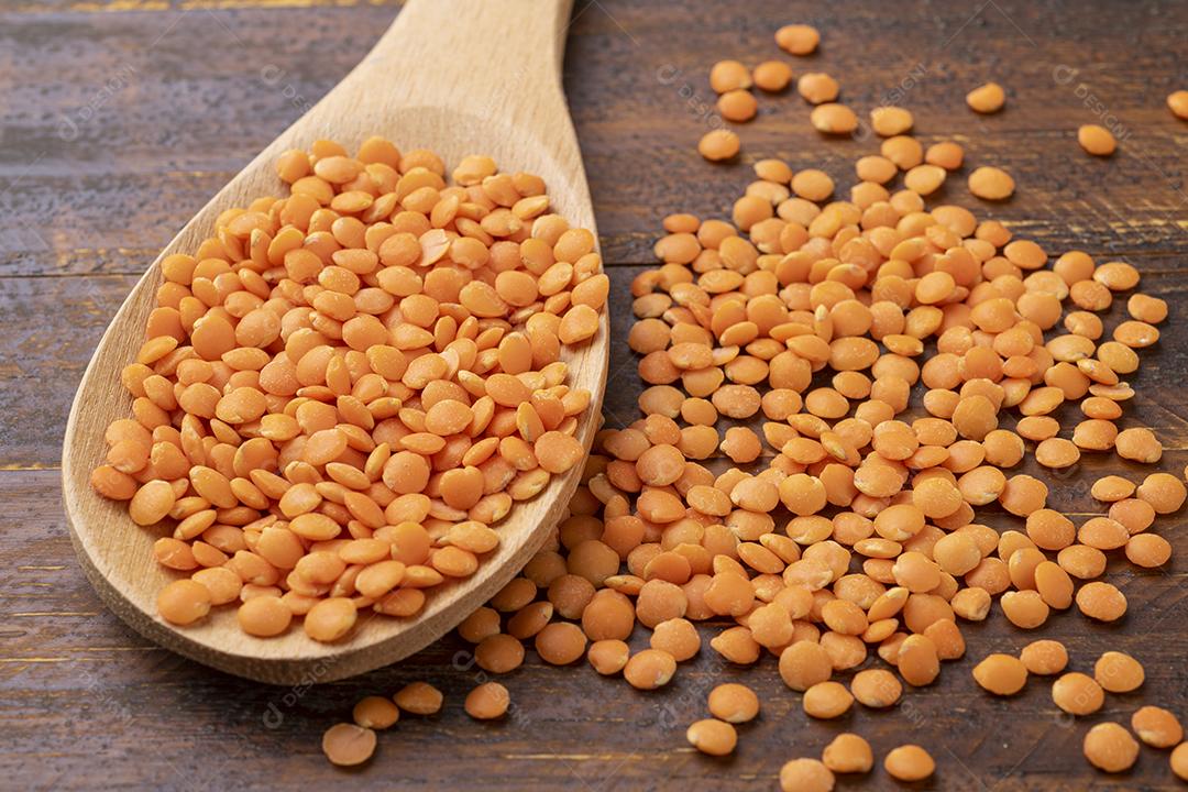 Lentilha de laranja em uma colher sobre mesa de madeira.