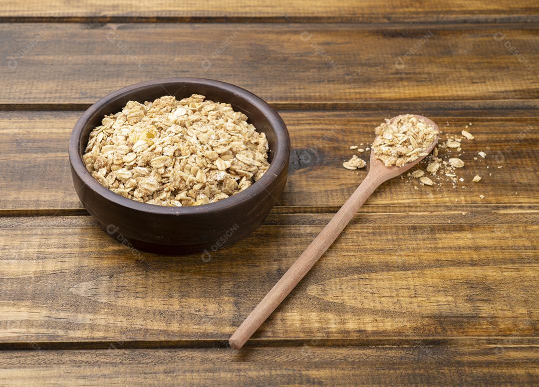 Granola ou muesli em uma tigela e em uma colher sobre mesa de madeira