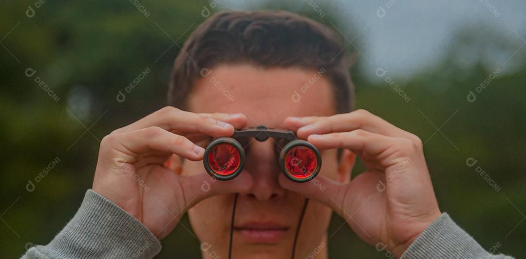 Jovem rapaz usando binóculos floresta