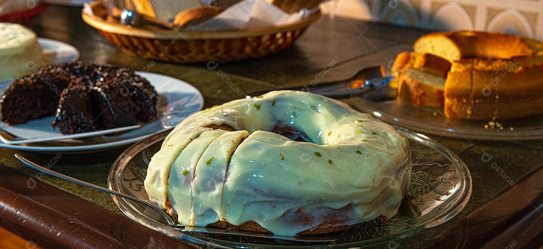 Café da manhã farto servido com bolos, tortas, geléias, bolos, queijo, presunto, café, leite.