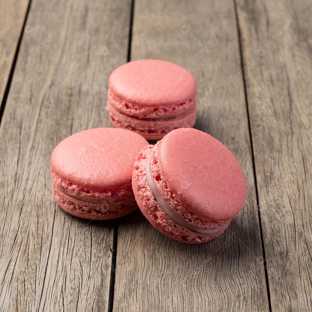 Três macarrons de frutas empilhados sobre mesa de madeira.