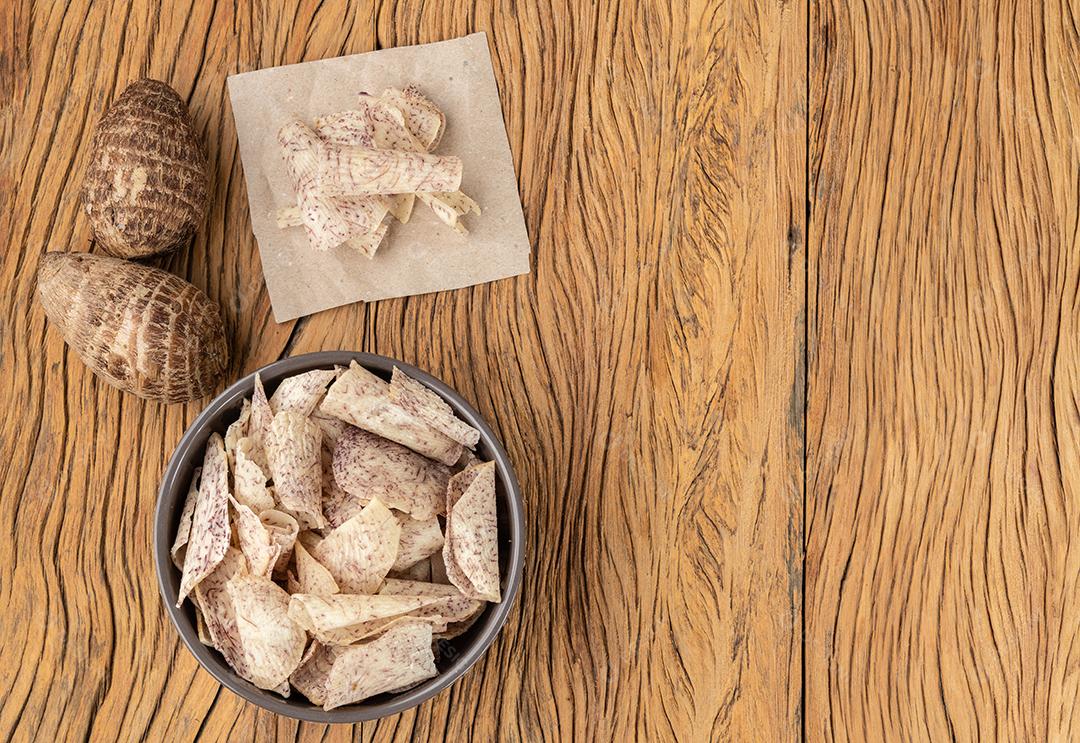 batatas fritas de taro em uma tigela com vegetais crus sobre mesa de madeira