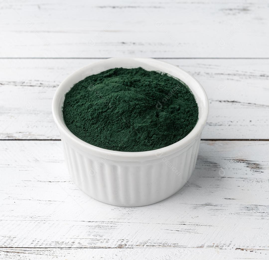 Pó de algas de espirulina em uma tigela sobre mesa de madeira.
