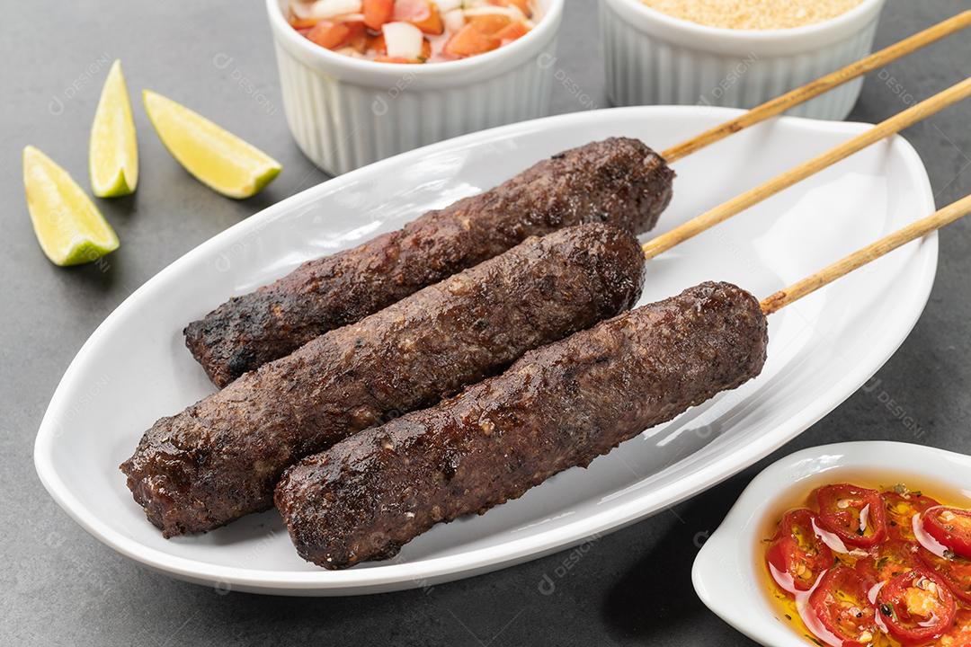 Espetos kafta com farofa, vinagrete sobre fundo de pedra.