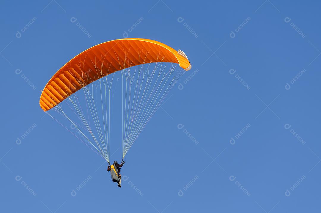 Laranja de parapente voando contra o céu azul. Esporte de aventura.