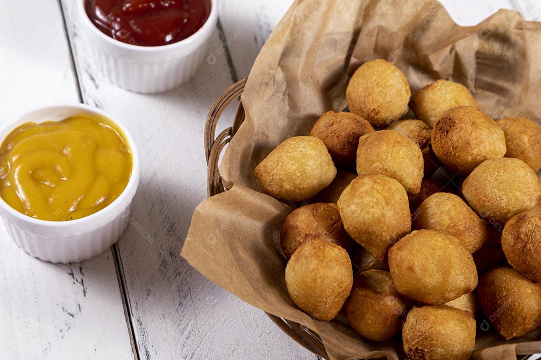 Salgados e ketchup em uma cesta com papel sobre mesa branca isolada