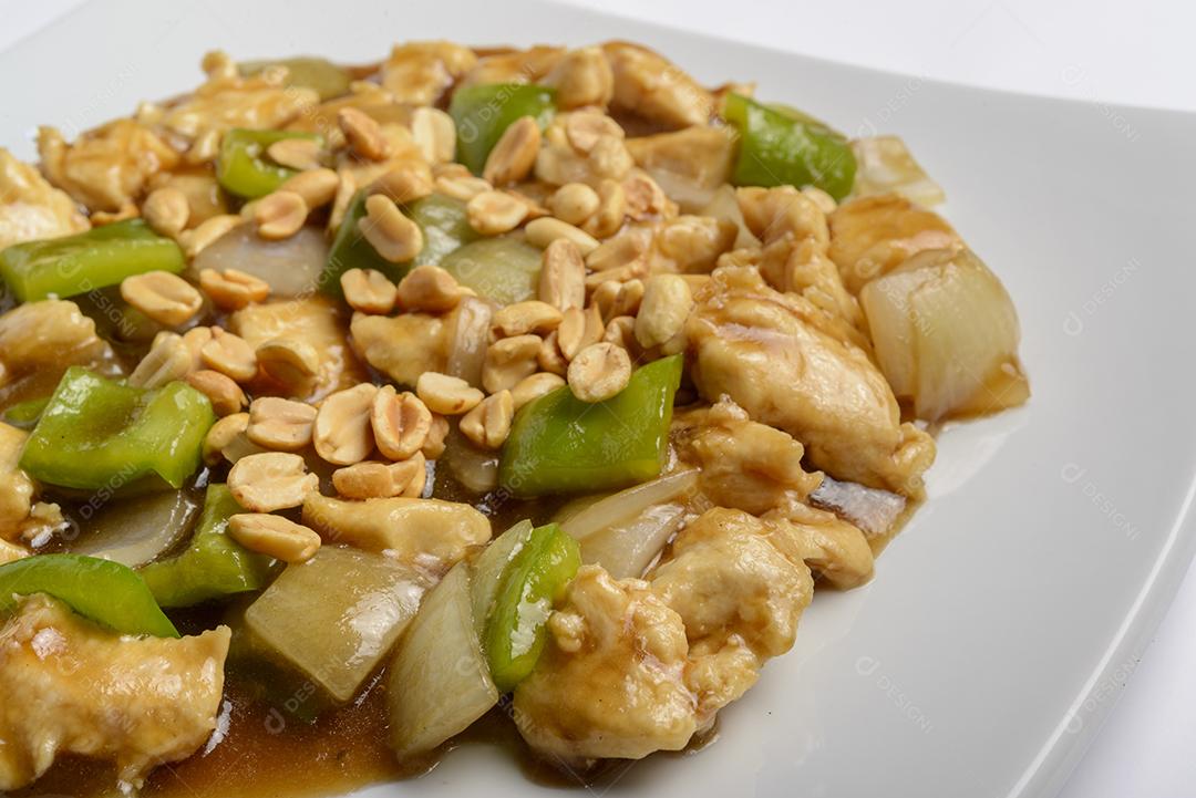 Frango de xadrez com pimentas verdes, cebolas e amendoins em prato branco isolado. Comida tradicional chinesa.