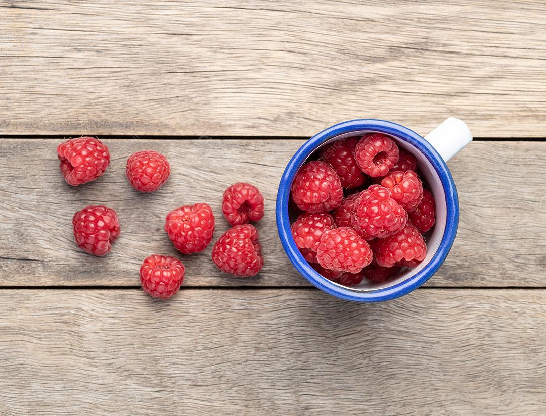 Um grupo de framboesas em um copo sobre a mesa de madeira.