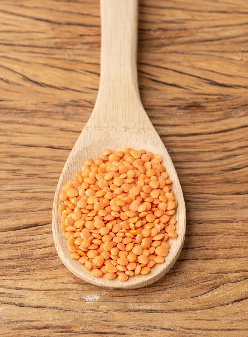 Lentilha laranja em uma colher sobre a mesa de madeira.