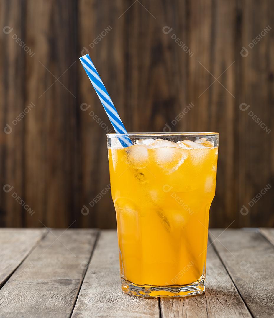 Refrigerante de laranja em um copo com gelo e palha sobre a mesa de madeira.
