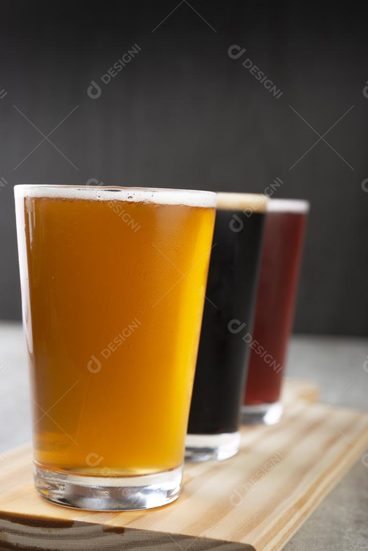 Três copos de cerveja sobre a placa de madeira. Dourado, escuro e r